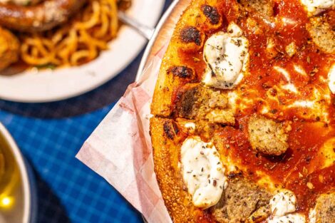 A pizza and a pasta dish from Colonial Pizza are shown on a blue tablecloth.