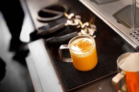 A latte is shown under an espresso machine.