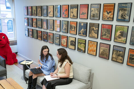 Students sitting under a collection of framed artwork and magazine covers.