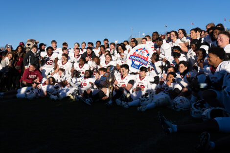 Football players smile holding a trophy and a sign that reads Football Champions.