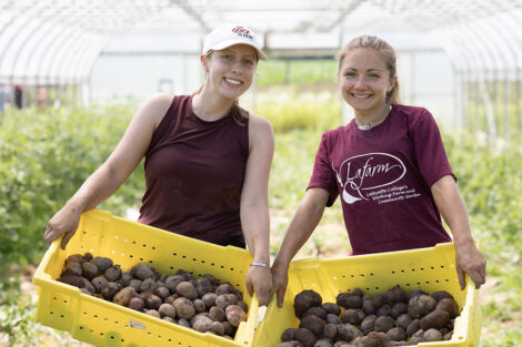 Students smile, holding buckets of potatoes.
