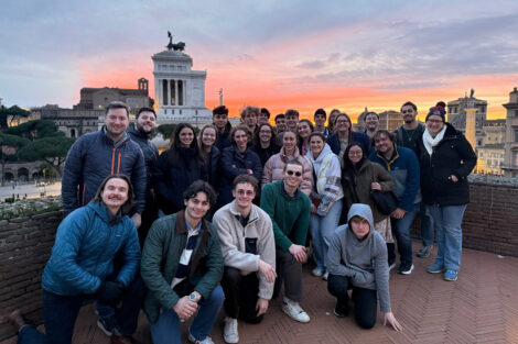 Students smile in front of a statue in Rome.