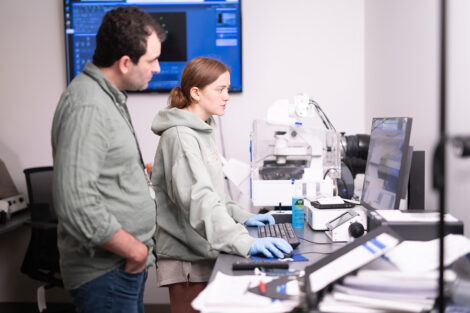 A student and faculty member conduct research at a computer in a lab.