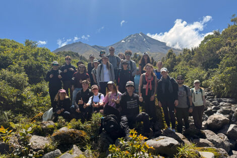 Students smile in front of a sweeping view of a mountain.